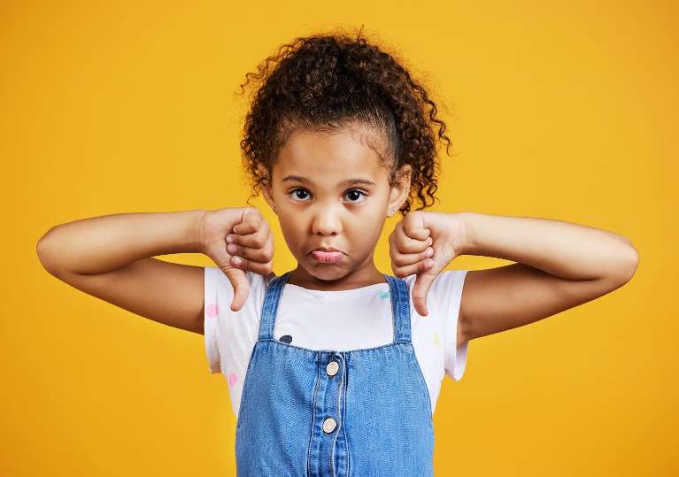 Black little girl gives 2 thumbs down against a yellow background