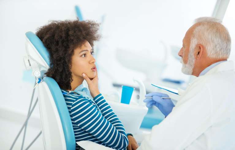 Black woman consults with her dentist while sitting in a dental chair holding her chin