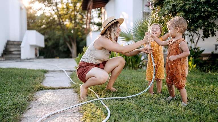 woman playing with toddlers in yard with hose during the summer